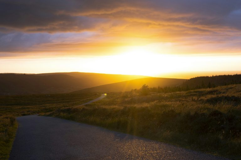 A moorland road at dusk through the Yorkshire moors with bare trees silhouetted against a dramatic stormy golden sky
